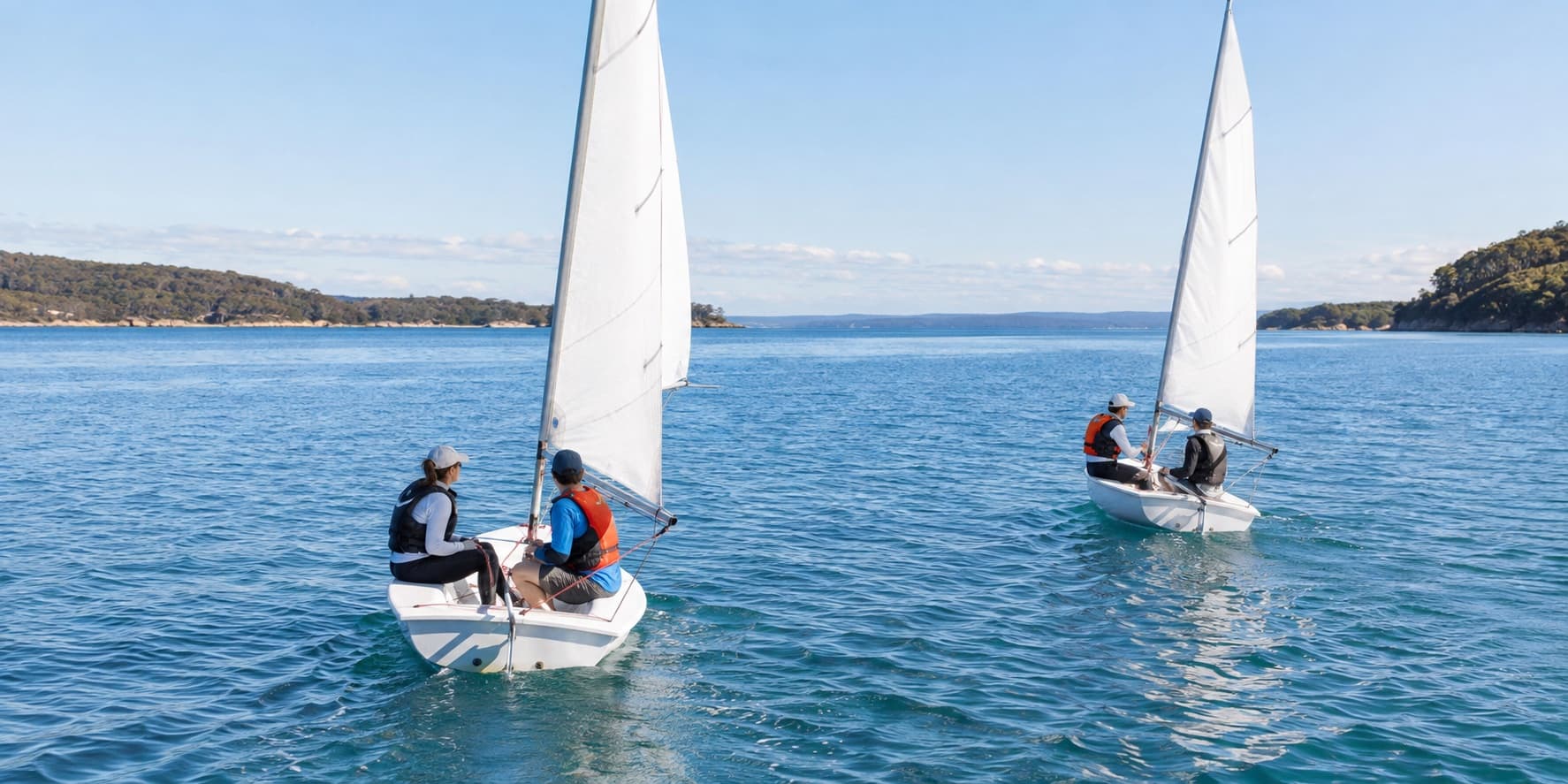Adult beginners practising sailing in two training dinghies on protected Australian water